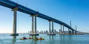 A large corporate group on a San Diego kayak tour near the Coronado Bridge and city skyline.